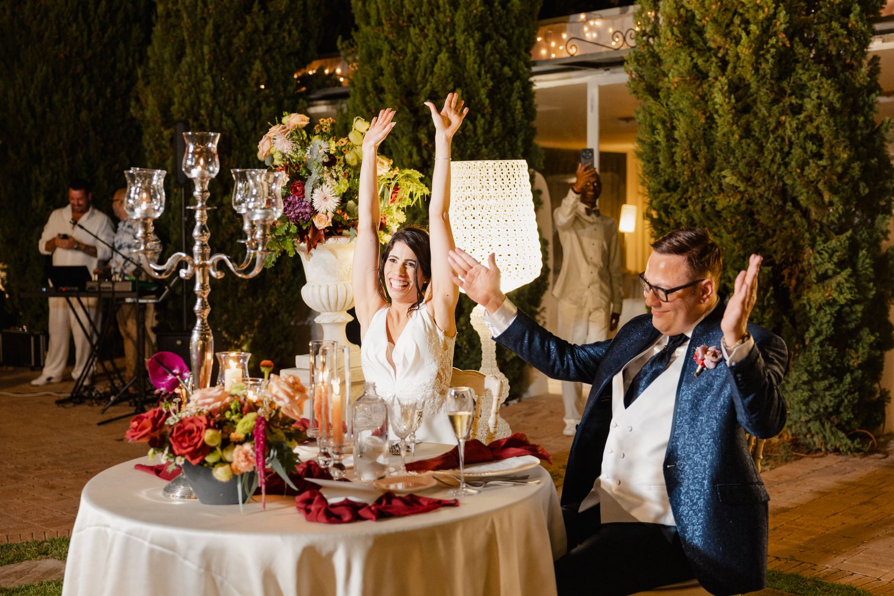 Una pareja celebrando su boda al aire libre entre flores y luces cálidas.