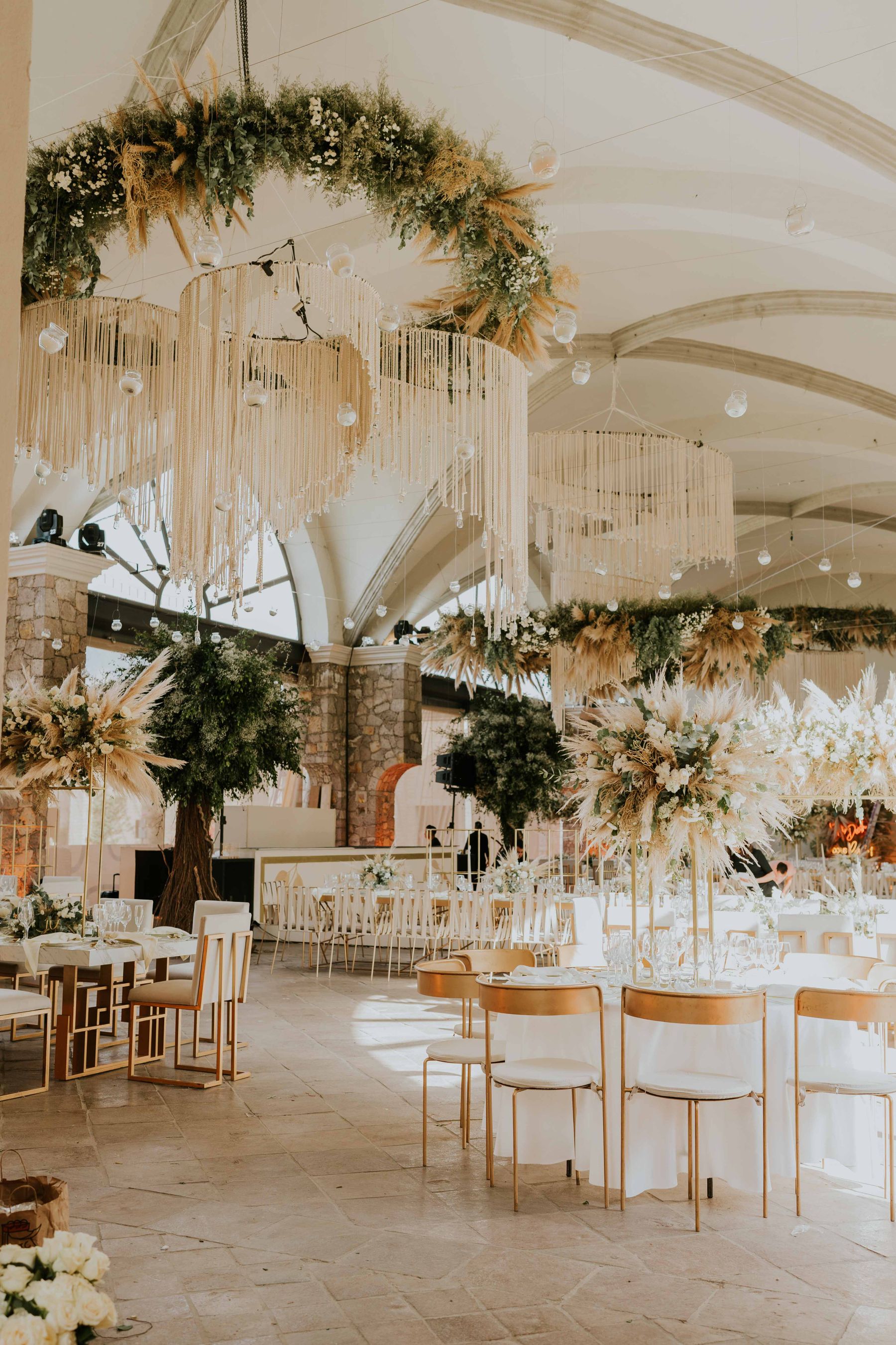 Un salón con instalaciones florales suspendidas, iluminación y mesas preparadas para un evento. Fotografía de inspiración.